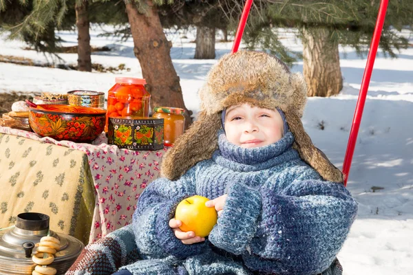 Menino em um boné com abas de ouvido joga parque de inverno. Estilo russo em um contexto de samovar e com bagels — Fotografia de Stock