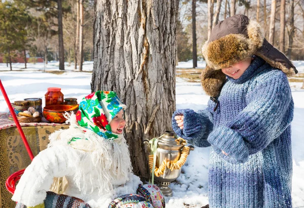 Copii în eșarfă rusească pavloposadskie pe cap cu imprimare florală pe zăpadă. Stilul rusesc pe un fundal de samovar și cu covrigi — Fotografie, imagine de stoc