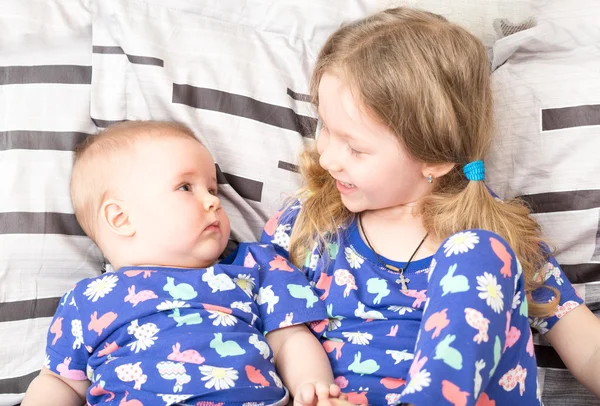 Two sisters. Older sister kid hugging his newborn little sister. Cute children girls on bed at home. — Stock Photo, Image