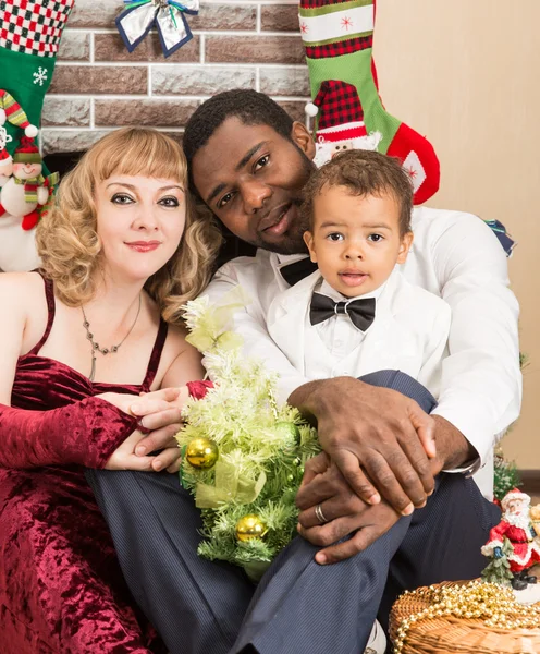 Lycklig familj: svart pappa, mamma och baby pojke vid öppna spisen. Jul och nyår — Stockfoto