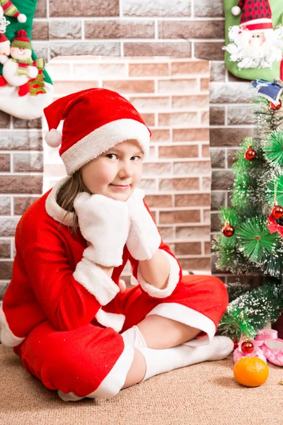 Meisje gekleed Santa Claus kostuum door open haard. Kerstmis en Nieuwjaar — Stockfoto