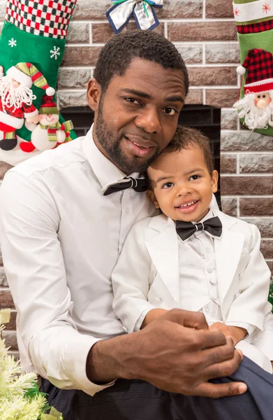 Feliz padre negro y niño abrazándose junto a la chimenea. Navidad y Año Nuevo —  Fotos de Stock