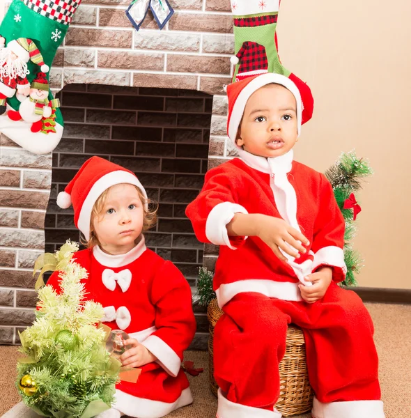 Niño afroamericano y niña vestido traje de Santa Claus junto a la chimenea. Navidad y Año Nuevo — Foto de Stock