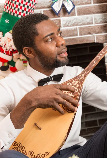 Uomo afroamericano con strumento musicale Dombra by fireplace. Natale e Capodanno — Foto Stock