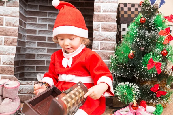 Liten flicka klädd kostym Santa Claus vid öppna spisen. Jul och nyår — Stockfoto