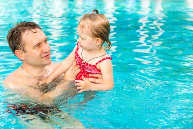 Tropikal tatil Havuzda yüzmek için yürümeye başlayan çocuk kızı öğretim etkin baba. Yaz tatillerini ve spor kavram