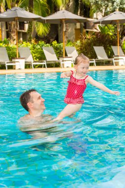 Tropikal tatil Havuzda yüzmek için yürümeye başlayan çocuk kızı öğretim etkin baba. Yaz tatillerini ve spor kavram