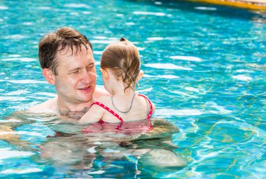 Tropikal tatil Havuzda yüzmek için yürümeye başlayan çocuk kızı öğretim etkin baba. Yaz tatillerini ve spor kavram