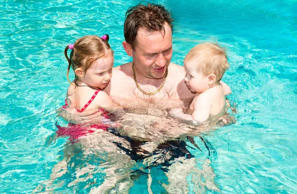 Active father teaching his children to swim in pool on tropical resort. Summer vacations and sport concept — Stock Photo, Image
