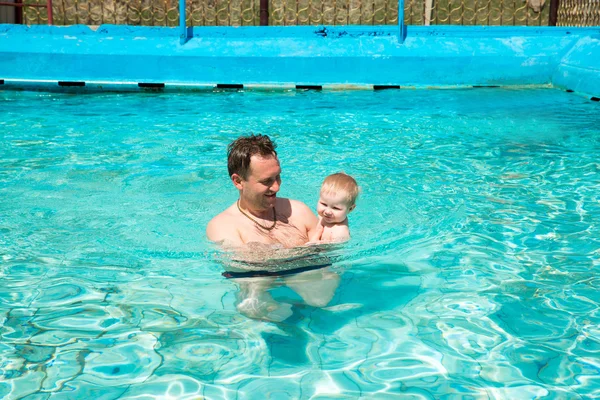 Active father teaching his child to swim in pool on tropical resort. Summer vacations and sport concept — Stock Photo, Image