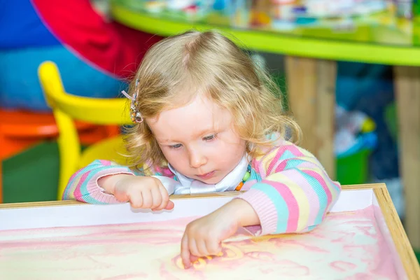 Симпатичная девочка рисует развивающийся песок в детском саду за столом в детском саду по методу Монтессори — стоковое фото