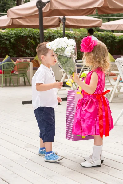 Il bambino di ragazzo dà fiori a bambino di ragazza durante compleanno. Piccola ragazza adorabile che festeggia 3 anni di compleanno. Infanzia. . — Foto Stock