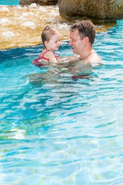 Tropikal tatil Havuzda yüzmek için yürümeye başlayan çocuk kızı öğretim etkin baba. Yaz tatillerini ve spor kavram