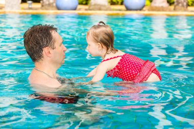 Tropikal tatil Havuzda yüzmek için yürümeye başlayan çocuk kızı öğretim etkin baba. Yaz tatillerini ve spor kavram
