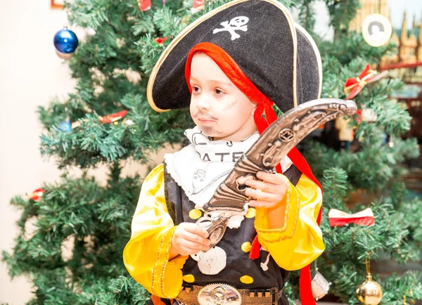 Ein kleiner Junge, der als Pirat zu Halloween auf dem Hintergrund des Weihnachtsbaums verkleidet ist. Kind in Faschingskostümen zu Weihnachten — Stockfoto