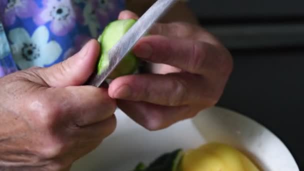 Fechar a casca e cortar pepino com faca em mãos enrugadas — Vídeo de Stock