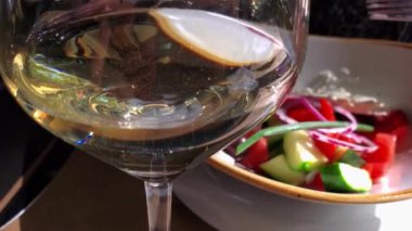 Cam kaplamalı parlak beyaz şarap. Odakları çözülmüş. Şarap kadehi aşırı yakın çekim, altın sıvıyla bulanık hareket, güneş ışığı.