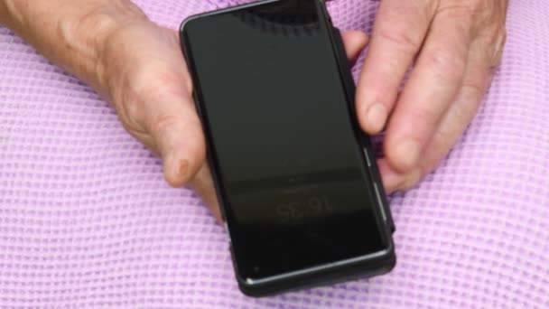 Telefone celular preto em mãos seniores femininas. Reflexões na superfície espelhada da tela do smartphone — Vídeo de Stock