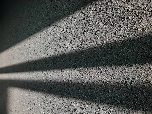 抽象幾何学的な影は 暗闇の中でスポットライトの光線のように見えます 灰色のステンドグラスの表面と光と影のストライプのラフ石膏壁 — ストック写真