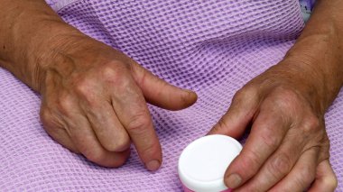 Kadın elleri, artrit parmaklarıyla küçük bir kavanoz nemlendirici kozmetik krem tutar. Yaşlı cilt bakımı konsepti. 80 yaşında el derisi yüzülmüş yaşlı bir kadın.