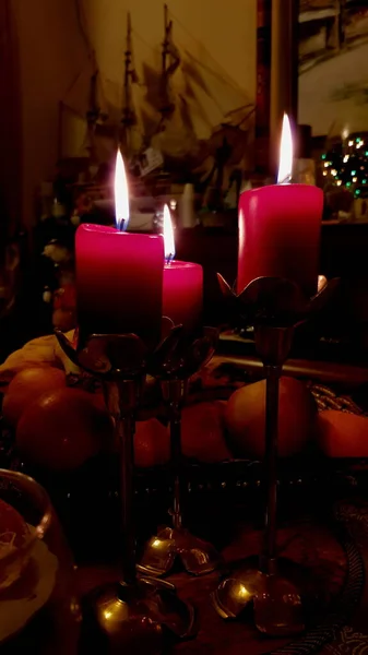 Still life with three red candles in vintage copper candelabras on dinner table in darkness. Candlelight flames of cylindrical red wax candles. Burning candlesticks on Christmas holiday table
