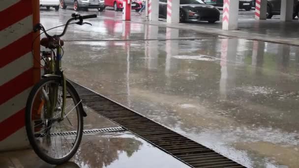 Verser la pluie par des flaques de stationnement urbain avec roue de vélo au premier plan et la circulation automobile à fond flou — Video