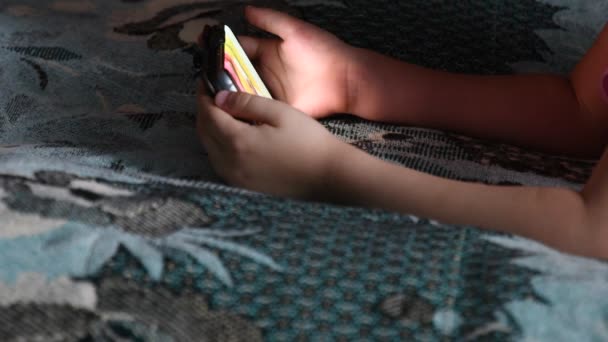 Маленькая девочка смотрит мультики на смартфоне держа гаджет в руках слишком близко — стоковое видео