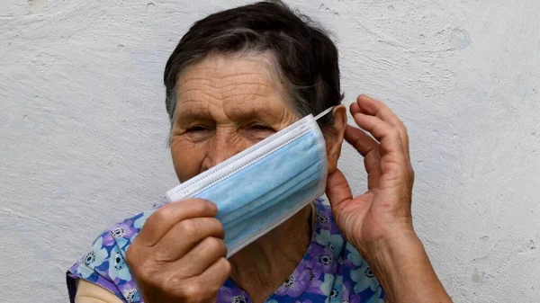 Velha senhora coloca máscara médica tocando sua orelha com os dedos — Fotografia de Stock