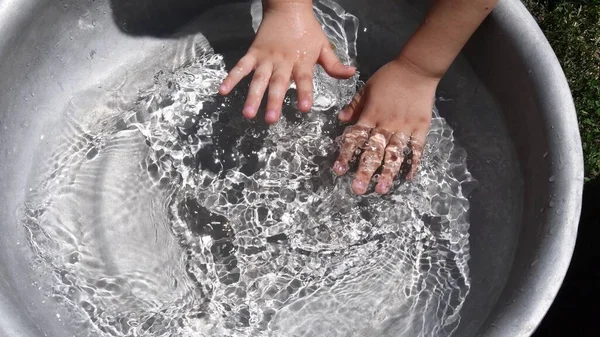 Miúdo a lavar as mãos em água limpa dentro da bacia. Diversão de verão — Fotografia de Stock
