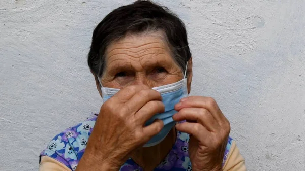 노부인이 주름 진 손으로 코에 있는 의료용 마스크를 고친다 — 스톡 사진