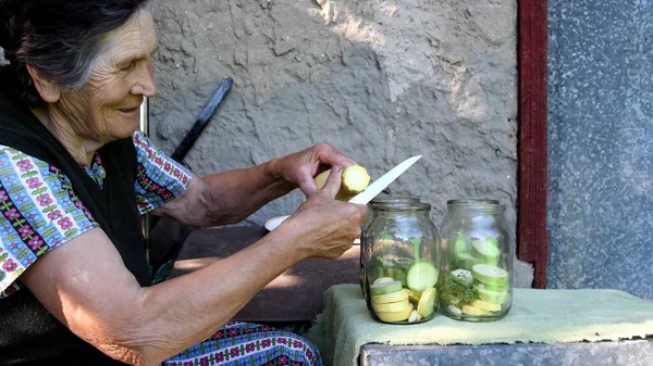 Пожилая женщина режет желтый сквош и кладет в банку — стоковое фото