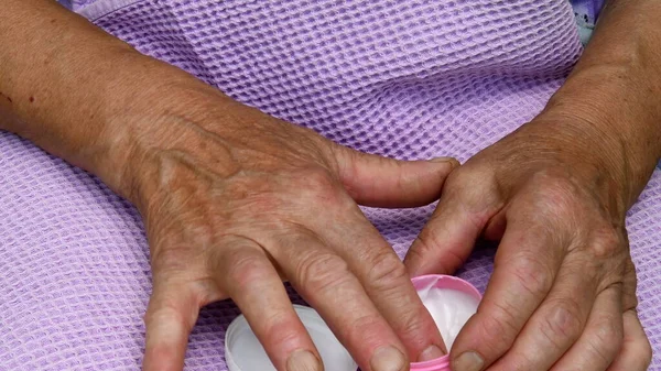 As mãos de velha senhora tomam a nata cosmética do pequeno jarro. Cuidados com a pele dos idosos — Fotografia de Stock