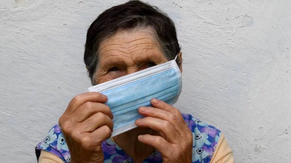 Velha senhora segura máscara médica com ambas as mãos para colocar em máscara em seu rosto — Fotografia de Stock
