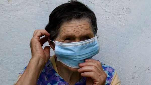 Old lady fixes protective mask on her ear and chin touching mask with hands — Foto Stock