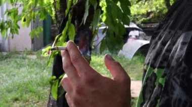 Arka bahçedeki arka planda erkek parmaklarıyla sigara içme.