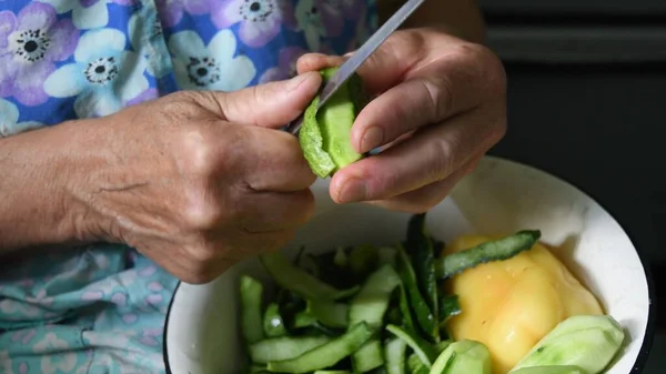 Closeup cutting cucumber peels with knife in wrinkled hands of senior woman — Stock Photo, Image