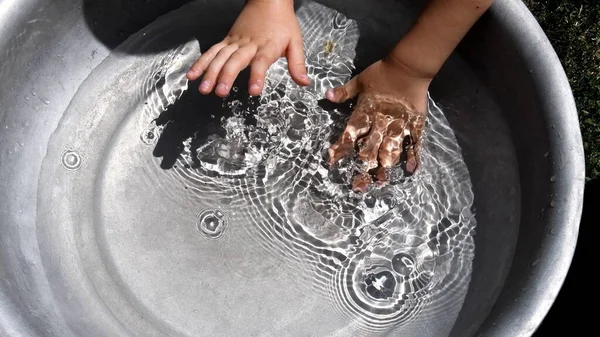 Miúdo salpicar as mãos em água limpa dentro da bacia. Diversão de verão — Fotografia de Stock