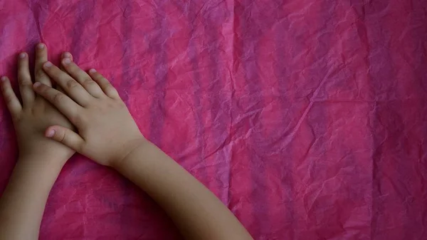 Хрещені руки маленької дитини на рожевому тлі з копіювальним простором — стокове фото