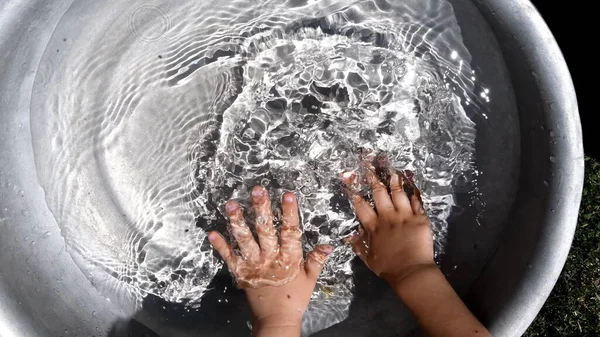 As mãos de criança desfocadas salpicam na água limpa dentro da bacia. Diversão de verão — Fotografia de Stock