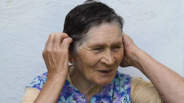 Ritratto di donna anziana sorridente che si tocca i capelli grigi con entrambe le mani per lisciare il suo taglio di capelli corto — Foto Stock