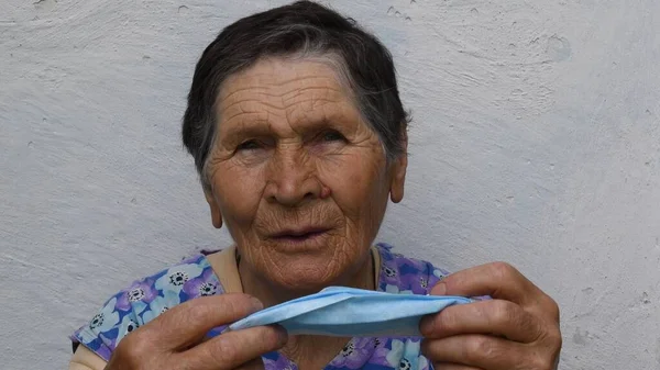Старша жінка знімає і складає одноразову маску зі зморщеного обличчя — стокове фото