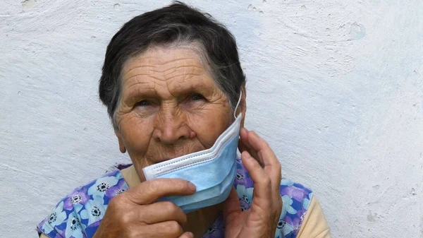 Mulher sênior tira máscara médica de uso único de seu rosto enrugado envelhecido — Fotografia de Stock