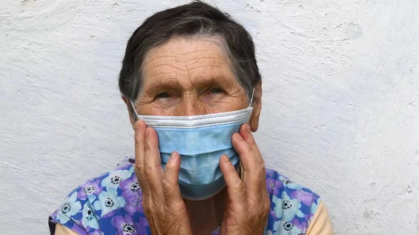 Старша жінка торкається одноразової маски на обличчі у віці з глибокими зморшками на лобі і біля очей — стокове фото