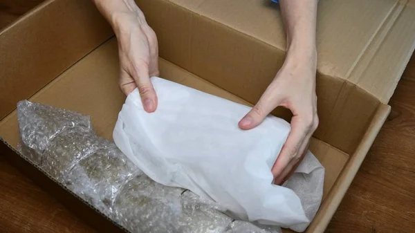 Packing up fragile tableware into plastic bubble wrapping inside cardboard box — Stock Photo, Image