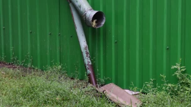 Summer rain pouring from old rusty gutter in front of green fence — Stock Video