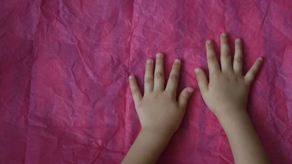 Вид зверху на руки дитини торкаються рожевого збитого паперу на столі з копіювальним простором — стокове фото