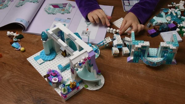 Тоддлер берет крошечного снеговика Lego и кладет его в ряд во время игры в блоки Lego из замороженного диснеевского мультфильма — стоковое фото