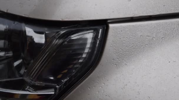 Närbild av bilhuven med regndroppar och strålkastare med suddiga reflektioner — Stockvideo