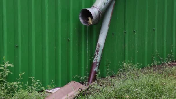 Autumn rain pouring from old rusty gutter in front of green fence — Stock Video