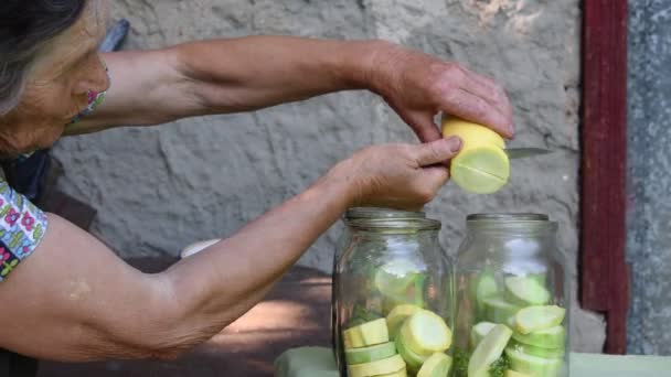 Старша жінка розрізає свіжі кабачки на скибочки і кладе всередину скляні банки для домашнього консервування — стокове відео
